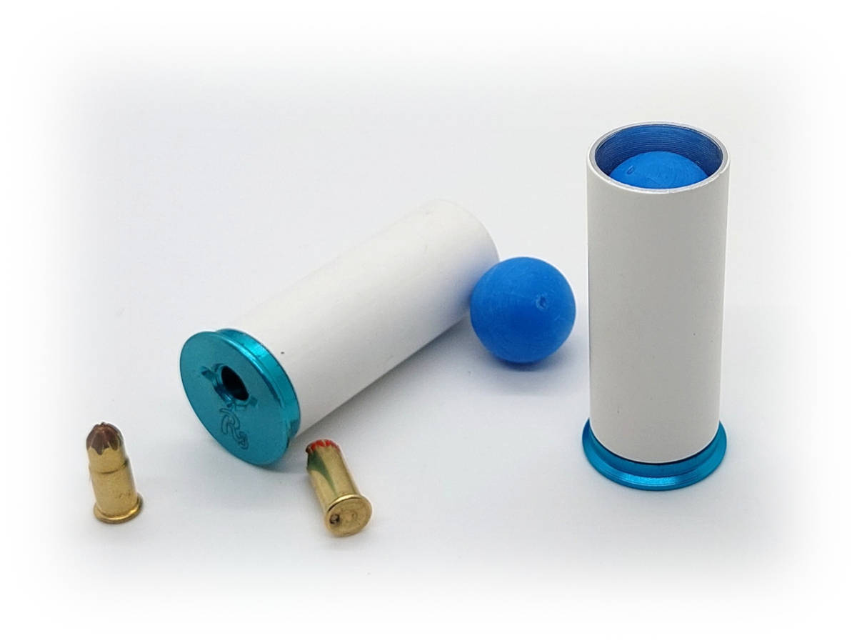 Exploded view of Ram-Shell components showing a reusable cartridge body, .22 blank charges, and a blue training projectile, alongside an assembled loaded cartridge